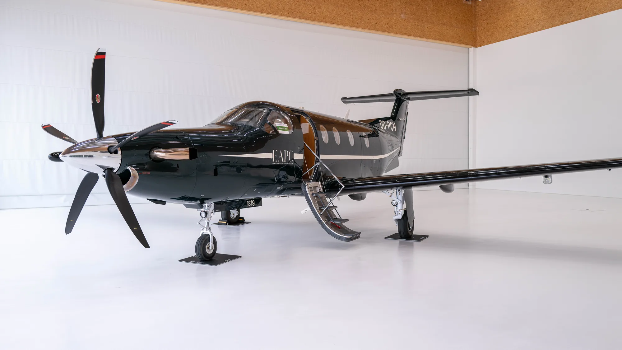 Pilatus PC-12 immatriculé OO-PCN, en livrée noire aux marques EAPC, dans un hangar.
